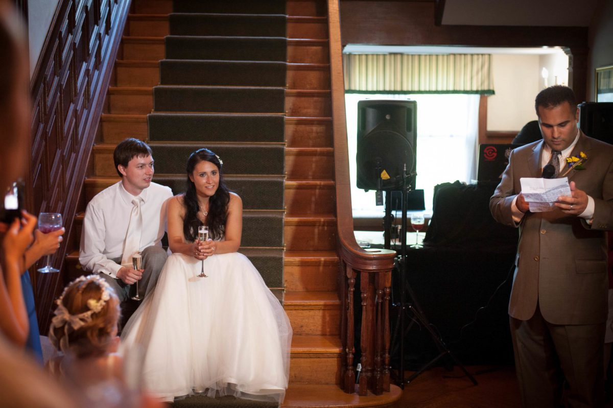 Toasts and Memories couple sitting on stairs while family member gives toast
